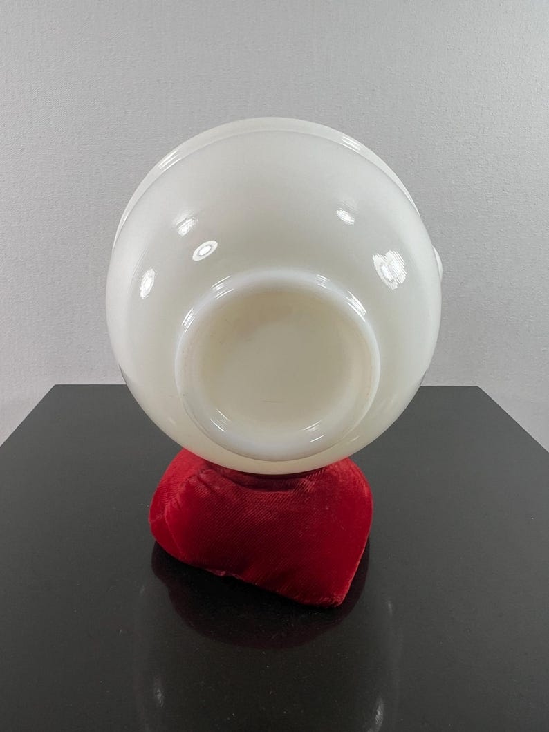 May include: A white milk glass bowl with a rounded shape, sitting on a red velvet cushion. The bowl is empty and the bottom is visible.
