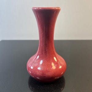 May include: A small, red ceramic vase with a rounded base and a narrow neck.