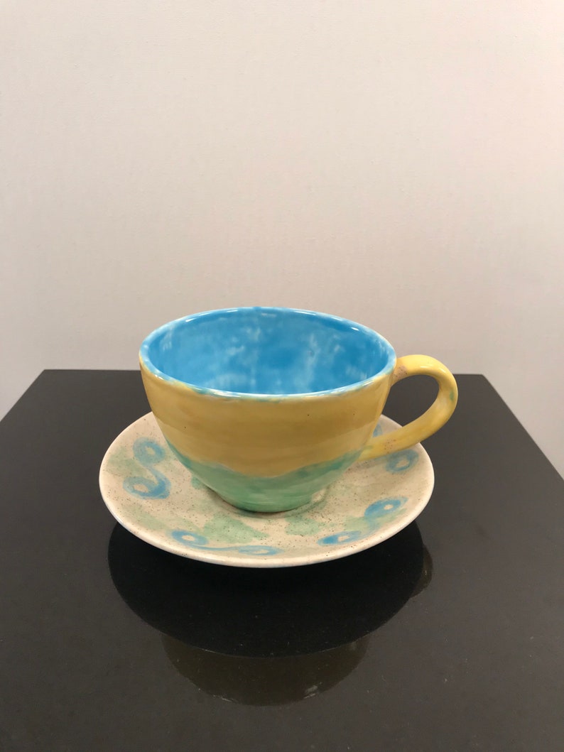 May include: A yellow and blue ceramic teacup and saucer set with a light blue interior and a white speckled design.