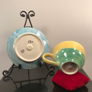 May include: A blue and white ceramic plate with a 13" diameter, and a yellow, green, and white ceramic mug with a 13" diameter. Both pieces are on a black surface.