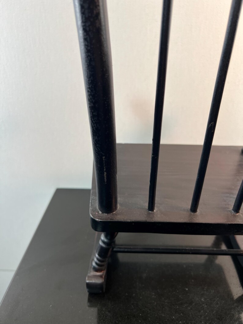 May include: Black wooden chair with a spindle back. The chair has a dark finish and a simple design. The chair is on a black surface. The chair is a decorative item.