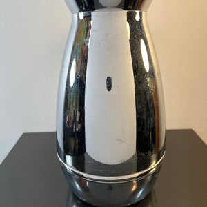 May include: A silver, polished, metal pitcher with a rounded body and a flared top.