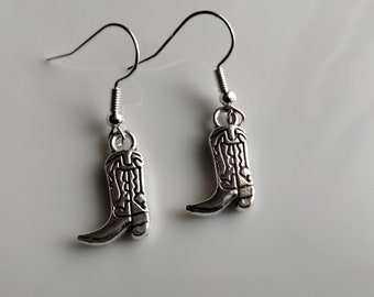 Pode incluir: Um par de brincos de prata com um amuleto de bota de cowboy.