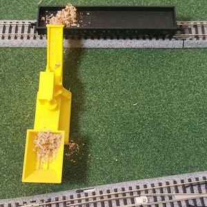 May include: A yellow toy train car with a wooden log inside. The car is being loaded by a yellow toy crane with a wooden log inside. The crane is on a green surface with a toy train track.