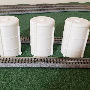 May include: Three white model train storage tanks with a black and silver model train car in the foreground.