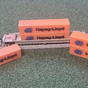 Peut inclure: Un ensemble de train miniature avec des conteneurs de fret orange portant l'inscription "Hapag-Lloyd". Les conteneurs sont empilés sur un wagon à plateau et certains sont au sol.