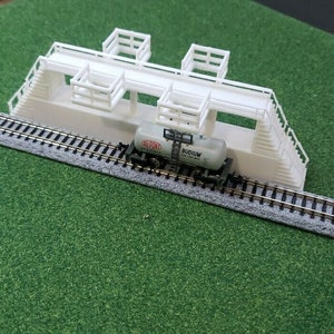 May include: White plastic model train trestle with a white tank car on the tracks. The tank car has red and black lettering that reads "DU PONT" and "BUDIUM TANK CONTENTS".