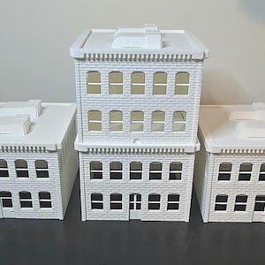 May include: Three white miniature buildings with windows and a flat roof. The buildings are made of plastic and are designed to look like city buildings.