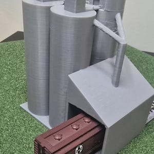 May include: A gray 3D printed model of a grain silo with a brown model train car pulling into the loading dock. The train car has the text "Santa Fe" on the side.