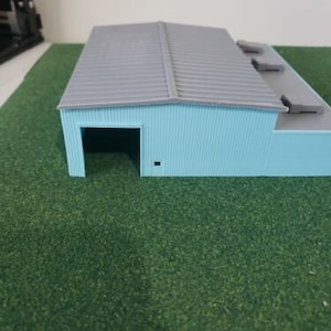 May include: A light blue model building with a gray roof and a single door opening. The building has a flat roof with a series of rectangular panels.