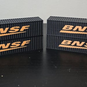 Könnte beinhalten: Vier schwarze Modellzug-Gütercontainer mit dem BNSF-Logo in Orange. Die Container sind in zwei Paaren gestapelt.