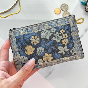 May include: A small blue and gold floral patterned fabric coin purse with a zipper closure.