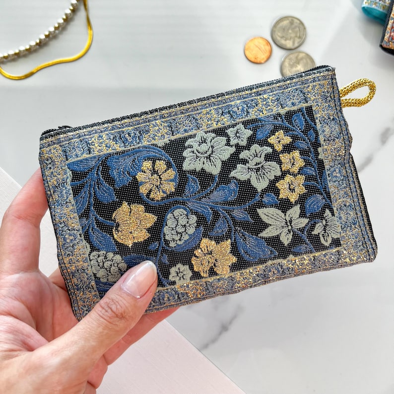 May include: A small blue and gold floral patterned fabric coin purse with a zipper closure.
