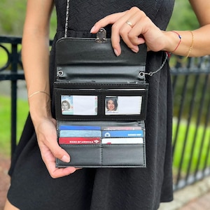 Op de afbeelding: Een zwarte leren portemonnee met een kettingband. De portemonnee heeft meerdere kaartsleuven en een transparant ID-venster. De portemonnee is open en toont een Bank of America creditcard en andere kaarten.