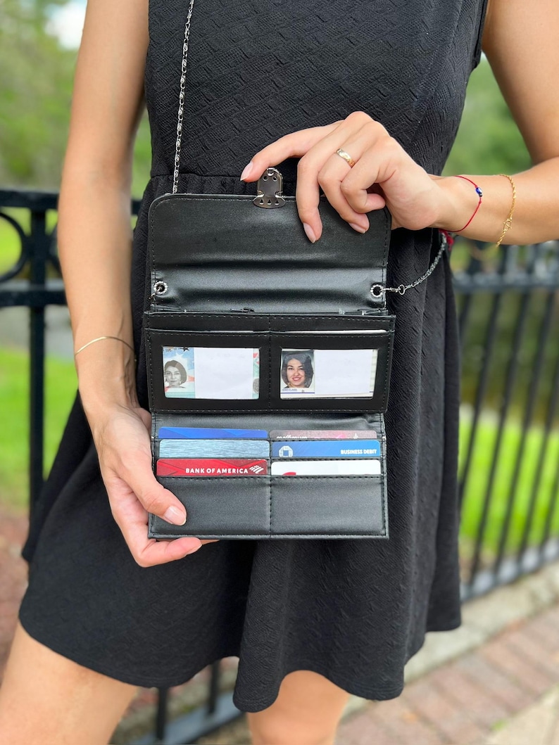 Op de afbeelding: Een zwarte leren portemonnee met een kettingband. De portemonnee heeft meerdere kaartsleuven en een transparant ID-venster. De portemonnee is open en toont een Bank of America creditcard en andere kaarten.