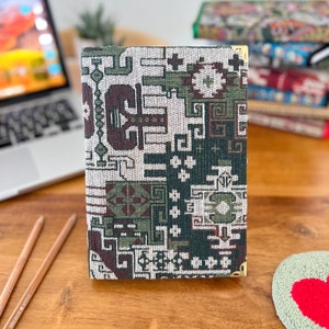 May include: A green, brown and white patterned notebook with gold accents. The notebook is closed and sitting on a wooden surface.