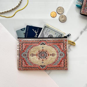 May include: A small zippered pouch with a colorful rug design. The pouch is open and contains cash and credit cards.