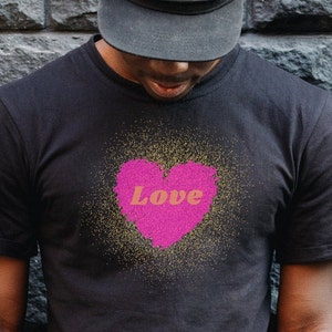 Pode incluir: Uma camiseta preta com um coração rosa e a palavra "Love" em letras laranja. O coração é rodeado por glitter dourado.