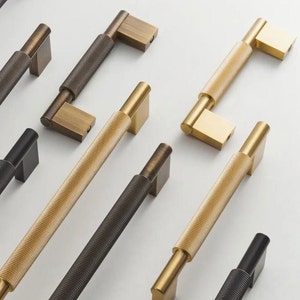 May include: Assortment of eight cabinet hardware pulls in various finishes, including black, brass, and bronze. The pulls have a textured, ribbed design.