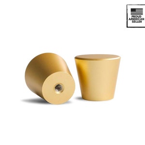 Puede incluir: Dos pomos de armario de color dorado con la parte superior redonda y una base ligeramente cónica. Los pomos tienen un agujero para tornillo en la parte inferior.