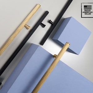 以下が含まれることがあります： 異なるスタイルのキャビネットプルが3つあります。2つは黒で、1つは金です。金色のプルはテクスチャ加工された表面を持っています。プルは薄い青色の表面に表示されています。