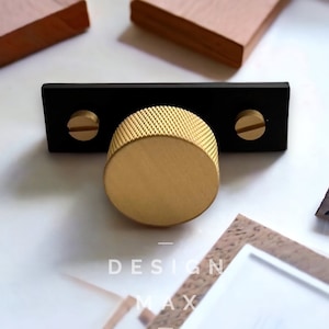 May include: A gold knob with a black rectangular base and two screws. The knob has a textured surface and a round shape.
