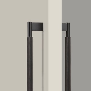 Może przedstawiać: Dwa czarne metalowe uchwyty do drzwi z fakturowanym uchwytem. Uchwyty są zamontowane na białej ścianie.