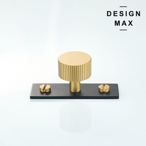 May include: A gold-toned cabinet knob with a ribbed design, mounted on a black rectangular base with two screws.