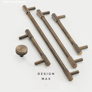 Puede incluir: Un juego de cinco tiradores de armario de latón antiguo con acabado texturizado. Los tiradores son de varios tamaños e incluyen un pomo redondo. El texto "DESIGN MAX" es visible en la imagen.