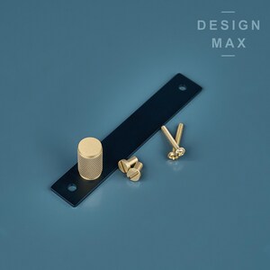 May include: A black metal drawer pull with a gold knob and screws. The pull is on a blue background with the text "DESIGN MAX" above it.