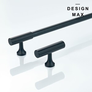 May include: Two black metal cabinet pulls with a ridged design. The larger pull is a bar handle, and the smaller pull is a T-shaped handle. The text "DESIGN MAX" is visible in the top right corner of the image.