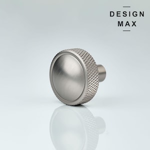 Peut inclure: Un bouton en métal argenté avec un bord texturé et moleté et un dessus lisse et arrondi. Le bouton est conçu pour être utilisé sur les armoires, les tiroirs ou les meubles.
