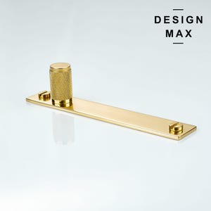 May include: Gold metal cabinet hardware with a rectangular plate and a round knob. The knob has a textured surface. The plate has two small screws on the bottom.
