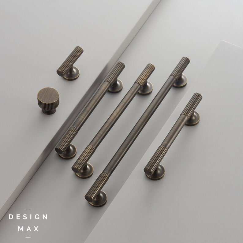 May include: A set of five antique brass cabinet pulls with a ribbed design. The pulls are arranged in a row on a white surface. The smallest pull is a knob.