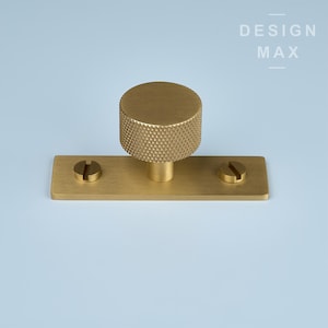 May include: A gold-toned cabinet knob with a textured round top and a rectangular base. The knob is attached to the base with two screws.