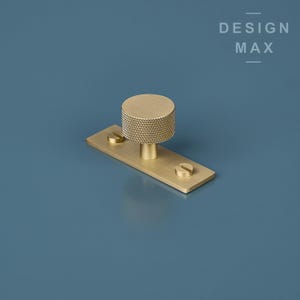May include: A gold-toned cabinet knob with a textured round top and a rectangular base. The knob is mounted on a blue surface.