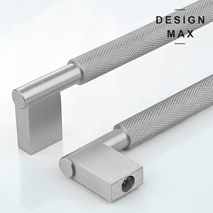 May include: Two silver cabinet door pulls with a textured finish. The pulls are L-shaped with a square base and a long, cylindrical handle. The text "DESIGN MAX" is printed on the image.