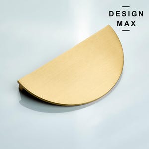 以下が含まれることがあります： ブラシ仕上げの金色半円形キャビネットプル。プルの上に黒文字でDESIGN MAXと印刷されています。