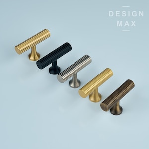 Può includere: Cinque pomelli per mobili diversi in fila su uno sfondo blu chiaro. I pomelli sono in metallo e hanno una forma a T. I pomelli sono nei seguenti colori: oro, nero, argento, ottone e bronzo. Il testo "DESIGN MAX" è nell'angolo in alto a destra dell'immagine.