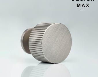 May include: A silver metal knob with a ridged design and a smooth, round top. The knob is designed for use on furniture or cabinets.