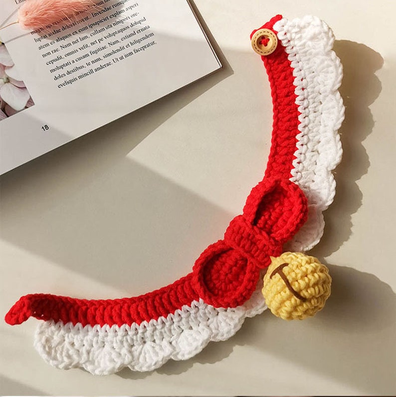 May include: Red and white crocheted pet collar with a bow and a yellow bell. The collar has a scalloped edge and a button closure.