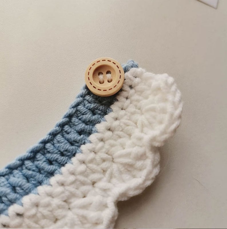 May include: A close-up of a crocheted collar with a white and blue striped pattern. The collar has a scalloped edge and a wooden button with two holes.