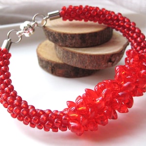 Könnte beinhalten: Ein rotes Perlenarmband mit einem silbernen Verschluss. Die Perlen sind spiralförmig angeordnet, mit einem Perlenhaufen in der Mitte.