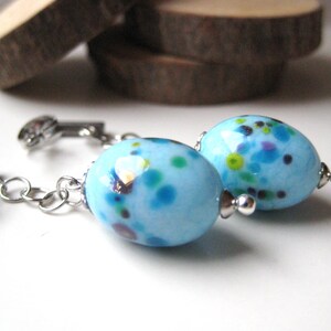 Peut inclure: Une paire de boucles d'oreilles avec des perles ovales tachetées de bleu et de vert, reliées à des chaînes et des fermoirs argentés.