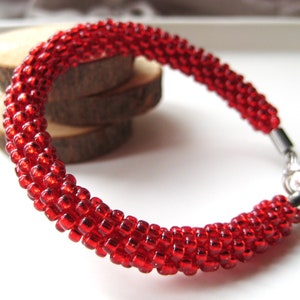 May include: A red beaded bracelet with a silver clasp. The bracelet is made of small, round beads that are tightly woven together.