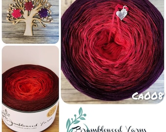 May include: A skein of ombre yarn in shades of purple, red, and orange. The yarn is wound into a ball and labeled "Bramblewood Yarns" with the code "CA008".