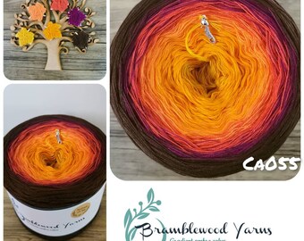 May include: A skein of ombre yarn in shades of brown, purple, orange, and yellow. The yarn is wound into a cake shape and labeled "CAOSS" and "Bramblewood Yarns Gradient ombre cakes".