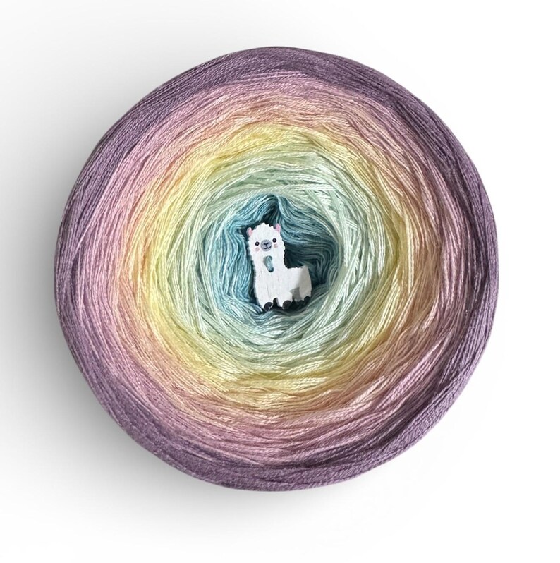 May include: A skein of yarn in a spiral pattern of pastel colors, including purple, pink, yellow, and blue. A small, white llama-shaped button is in the center of the yarn. The yarn is likely for knitting or crochet projects.
