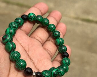 May include: A green and black beaded bracelet with a silver charm. The bracelet is made of malachite and onyx beads.