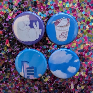 May include: Four round pins with different designs. One pin features a white cat curled up, another has a blue sky with white clouds, another has a cityscape with tall buildings, and the last pin has a cartoon cup of noodles with the text "Copy Noodle".